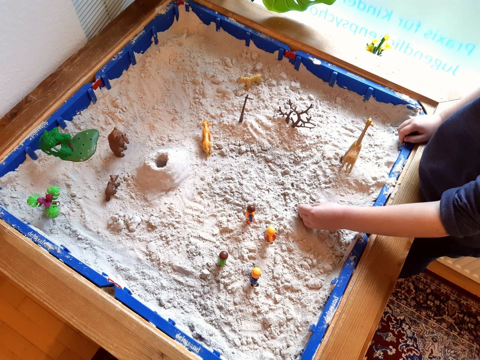 ein Sandkasten, in dem ein Kind mit Spielfiguren spielt;